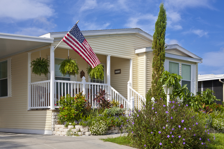 Photo of a manufactured home in a community with a front entry porch displaying an American flag