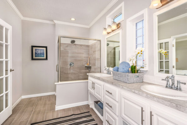 This large master bathroom has a walk-in diplomate tile shower. The cabinets are white with his and her sinks. Horizontal windows let in lots of light. The French doors add an elegant look to the bathroom